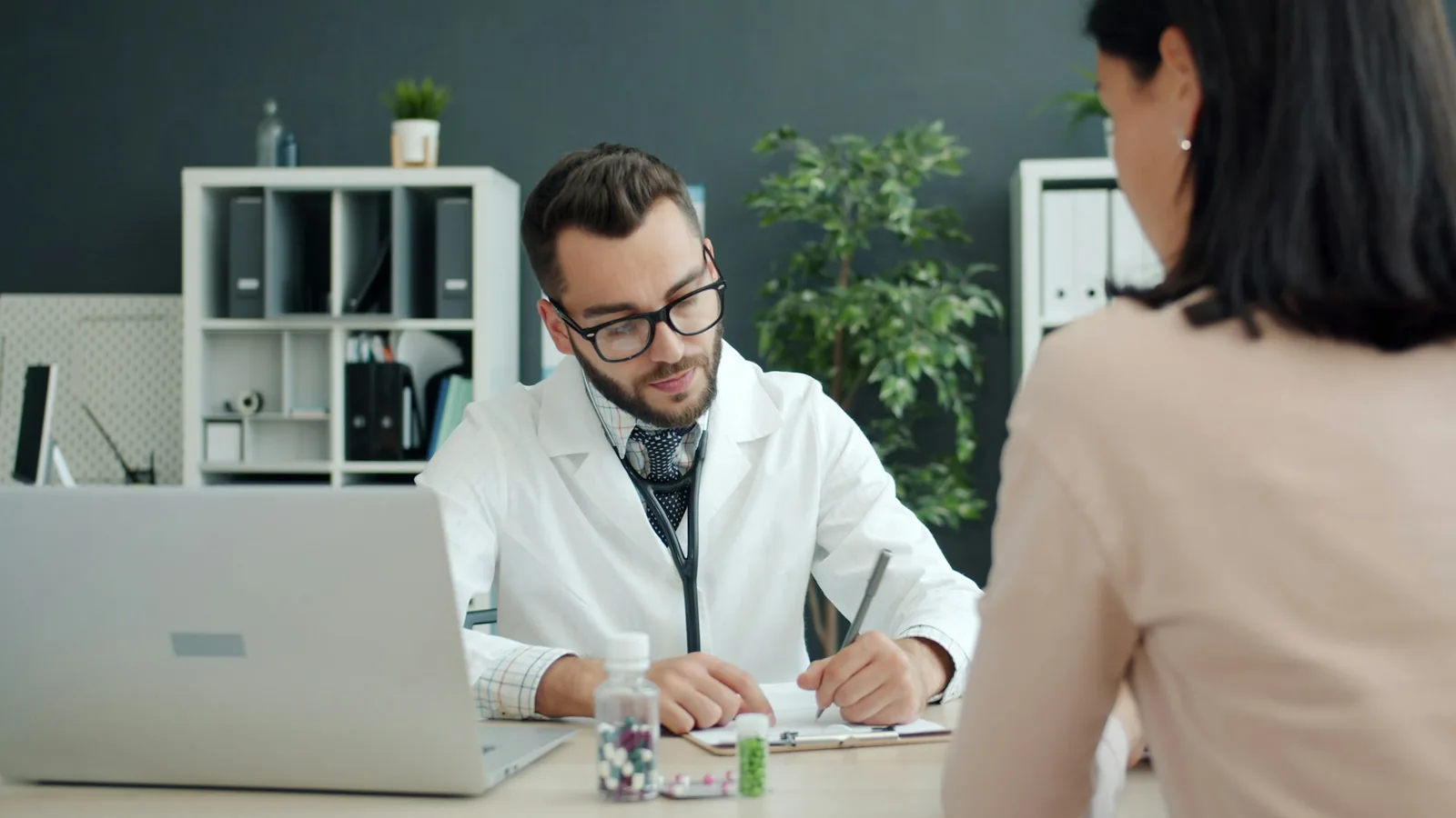 En läkare antecknar vid sitt skrivbord medan en patient sitter mittemot